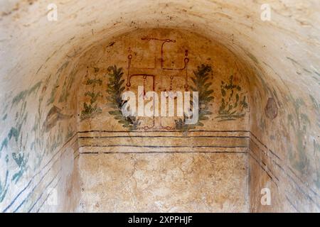 Fresque byzantine d'une croix entourée de branches d'oliviers dans un ancien tombeau chrétien, mettant en valeur le symbolisme religieux et l'art historique Banque D'Images