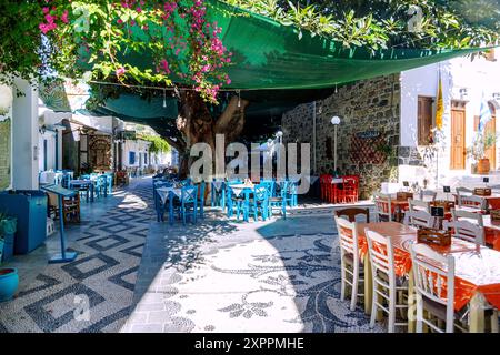 Place du village Platía Ilikioméni avec des tavernes et de l'ombre des arbres à Mandráki sur l'île de Nissyros (Nisyros, Nissiros, Nisiros) en Grèce Banque D'Images