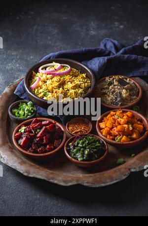 Un assortiment de plats indiens pakistanais végétariens vibrants et savoureux, y compris le riz biryani, servis dans de petits bols en bois sur un plateau rustique Banque D'Images