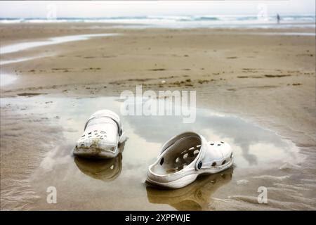 perdu vieilles chaussures couchées dans l'eau sur la plage, retrouvées et laissées Banque D'Images