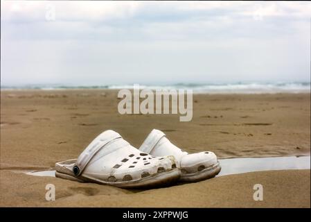 perdu vieilles chaussures couchées dans l'eau sur la plage, retrouvées et laissées Banque D'Images