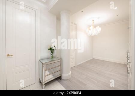 Hall d'entrée de la maison de luxe. Intérieur. Porte de chambre fermée en bois, plancher brun. Minimalisme. Voyant LED. Ouvrir la cuisine en arrière-plan. Lampe de luxe. Banque D'Images