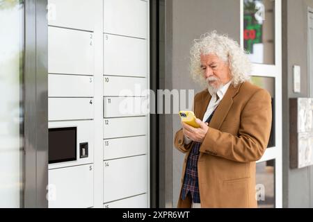 Homme plus âgé avec un paquet dans un casier, regardant son téléphone intelligent Banque D'Images