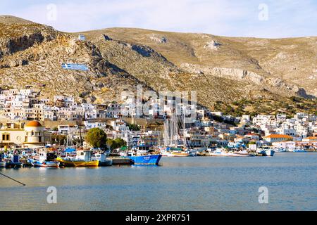 Capitale de l'île Póthia, chapelle blanche, drapeau grec, maisons aux couleurs pastel et bateaux dans le port sur l'île de Kalymnos (Kalimnos) en Grèce Banque D'Images