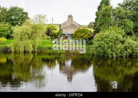 Grassington Yorkshire UK-27 juillet 2024. Chalet de campagne pittoresque avec une végétation luxuriante reflétée sur une rivière tranquille. Banque D'Images