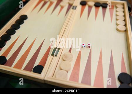 Gros plan d'une planche de backgammon traditionnelle en bois, avec des pièces noires et blanches et deux dés, prêt pour un match. Banque D'Images