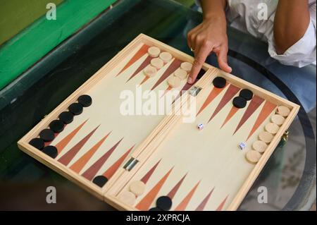 Une image en gros plan montrant des gens jouant au backgammon sur une planche de bois, avec des mains déplaçant des morceaux et des dés en vue. Idéal pour illustrer la stratégie, lei Banque D'Images