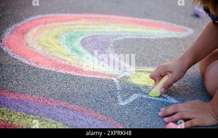 Les enfants dessinent un arc-en-ciel sur l'asphalte avec de la craie colorée. Trottoir. Activités en plein air pour les enfants. Dessin et peinture. Main. Fond de terrain de jeu scolaire Banque D'Images