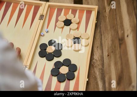 Gros plan d'une partie de backgammon jouée à l'extérieur sur une table en bois, avec des dés et des dames dans un match captivant. Banque D'Images