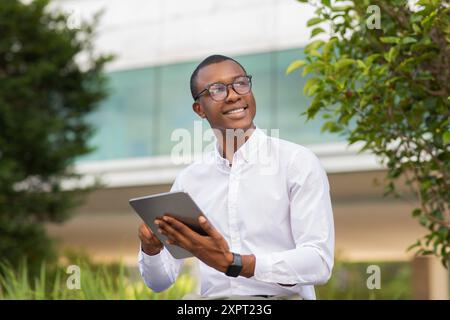 Jeune homme souriant tout en utilisant Tablet dans l'espace urbain extérieur Banque D'Images