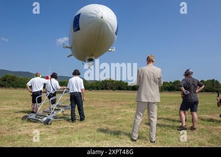 Dirigeable utilitaire rempli d'hélium Zeppelin NT atterrissant en France. Les membres d'équipage au sol dans un champ pendant une journée ensoleillée supervisent l'opération d'atterrissage du dirigeable. Banque D'Images