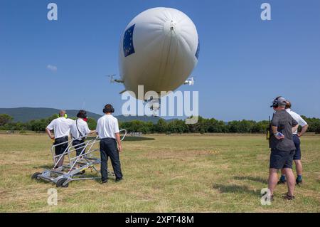 Le dirigeable Utility Zeppelin NT capturé lors d'un atterrissage en France. L'équipage au sol assiste le dirigeable rempli d'hélium lorsqu'il descend vers le site d'atterrissage par temps clair. Banque D'Images