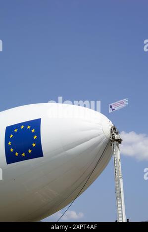 Le dirigeable Utility Zeppelin NT, une classe de dirigeables remplis d'hélium, est amarré en France sous le drapeau de l'Union européenne. Capturée sur un ciel bleu vif, la scène met en valeur la technologie aéronautique moderne. Banque D'Images