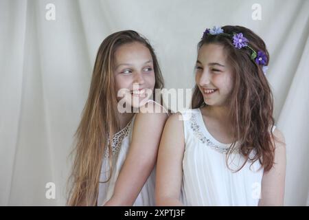 deux filles preteen joyeuses portant des robes blanches sur fond clair Banque D'Images