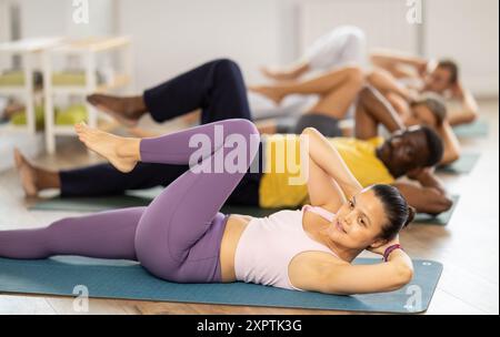Femme asiatique effectue des exercices pour renforcer les muscles abdominaux pendant l'entraînement multinational de groupe Banque D'Images