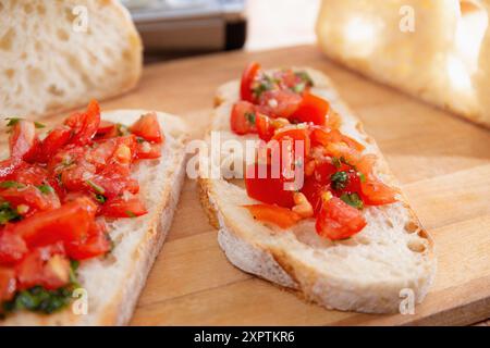 Gros plan de la bruschetta de tomates sur des tranches de pain artisanales, avec des tomates fraîches hachées et des herbes sur une planche de bois. Banque D'Images