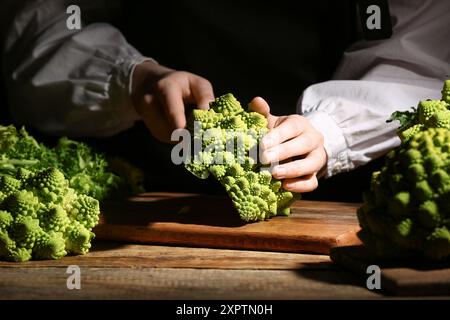 Femme coupant le brocoli Romanesco frais sur fond sombre, gros plan Banque D'Images