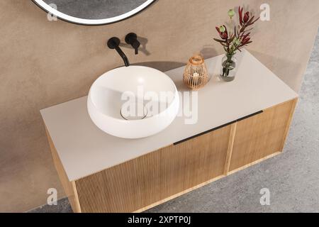 Un lavabo de salle de bain avec un bol blanc et un robinet noir. Un vase avec des fleurs rouges se trouve sur le comptoir à côté de l'évier Banque D'Images