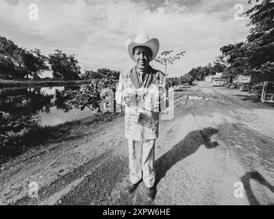 Jhon Smith Noriega pose pour un portrait à côté du canal supérieur à Laguna del Nainari dans la ville de Obregón, Sonora, Mexique le 14 juillet 2024. Jhon porte un costume du groupe de musique populaire ou régionale la Banda appelé lLaberinto tout en demandant un soutien financier avec un bateau à l’image de la Vierge de Guadalupe pour “Mi Casa Albergue” (photo Luis Gutiérrerez / Norte photo) Jhon Smith Noriega posa para un retrato junto al canal alto en la Laguna del Nainari en ciudad Obregón Sonora México el 14 julio 2024. Jhon viste de traje de la agrupación de músical Popular o Regional de la Banda Banque D'Images