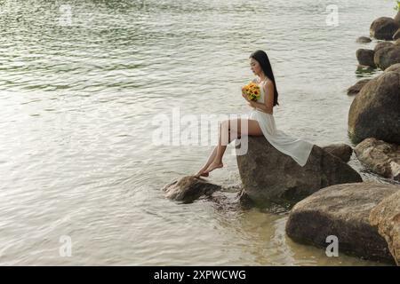 Femme asiatique en robe blanche dans la solitude par les rochers de bord de mer Banque D'Images