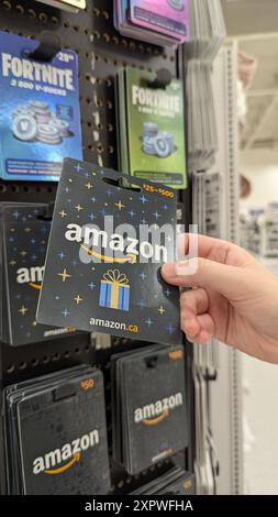 Une femme tenant une carte cadeau Amazon devant un affichage flou de cartes cadeaux dans un supermarché. Banque D'Images