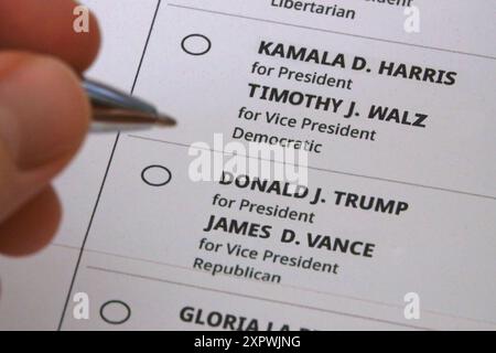 Une main tenant un stylo est montrée planant entre les bulles pour voter pour Kamala Harris et Tim Walz ou Donald Trump et JD Vance sur un bulletin de vote postal. Banque D'Images