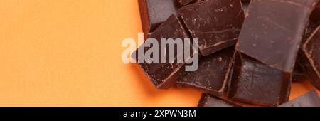 Morceaux cassés de barre de chocolat amer foncé sur un fond de couleur orange. Copier l'espace Banque D'Images