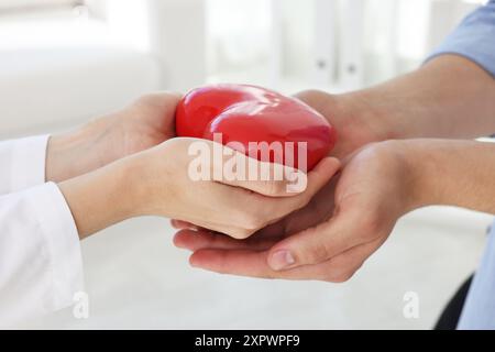 Docteur donnant le coeur rouge au patient à la table blanche en clinique, gros plan Banque D'Images