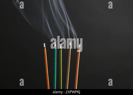 Bâtons d'encens aromatiques fumant sur fond noir Banque D'Images