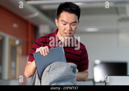 Gros plan d'un jeune étudiant adolescent qui emballe divers articles dans son sac à dos dans une salle de classe Banque D'Images