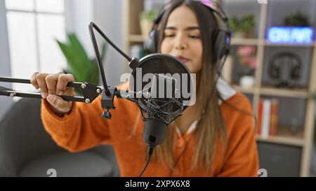 Une jeune femme hispanique portant des écouteurs parle dans un microphone de studio, indiquant un podcast intérieur ou une session de radio. Banque D'Images