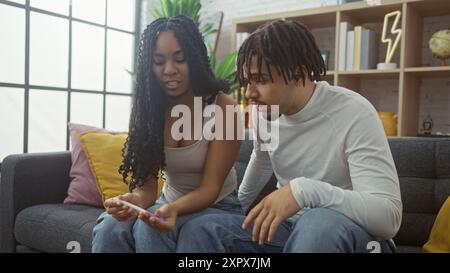 Un couple d'attente examine un test de grossesse ensemble dans leur salon confortable, réfléchissant à leur future famille potentielle. Banque D'Images