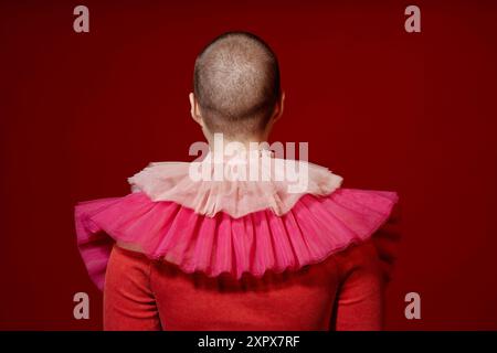 Vue arrière minimale de la jeune femme avec buzzcut portant une robe rouge élaborée avec volants espace de copie Banque D'Images