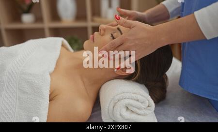 Une femme reçoit un massage facial relaxant d'un thérapeute dans une salle de spa paisible avec un éclairage doux et un environnement confortable. Banque D'Images