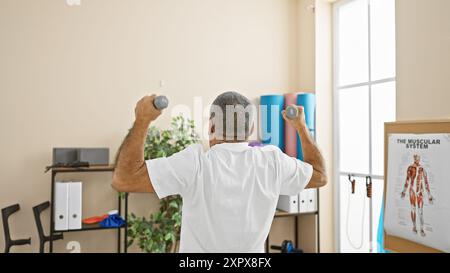 Homme hispanique mature s'exerçant avec des haltères dans la salle de rééducation d'une clinique de physiothérapie. Banque D'Images