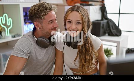 Un homme et une femme avec des écouteurs dans un studio de musique moderne partagent un moment joyeux ensemble. Banque D'Images