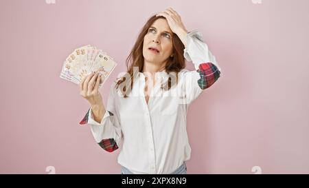 Une femme d'âge moyen inquiète tient la lire turque, contemplant les finances contre le mur rose Banque D'Images