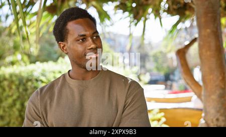 Homme afro-américain contemplatif profitant d'un moment de sérénité dans un parc luxuriant de la ville. Banque D'Images