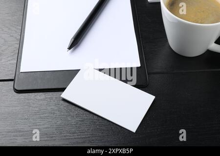 Cartes de visite vierges, presse-papiers avec feuille, stylo et tasse sur table en bois noir. Maquette pour le design Banque D'Images