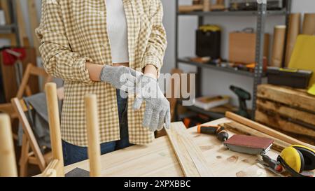 Une femme portant des gants de sécurité se préparant à travailler sur un projet de menuiserie dans un atelier. Banque D'Images