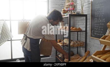 Jeune homme magasinant à la boulangerie, sélectionnant le pain de l'étagère dans un cadre élégant de magasin intérieur. Banque D'Images