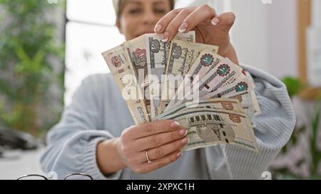 Jeune femme hispanique tenant des livres égyptiennes dans un bureau intérieur bien éclairé. Banque D'Images