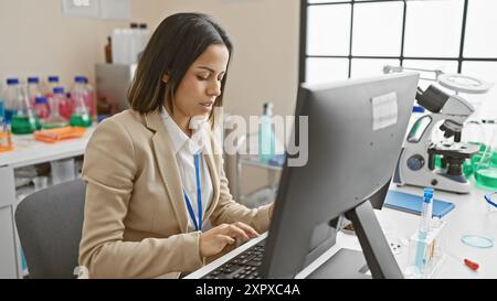 Scientifique hispanique ciblée utilisant l'ordinateur dans un laboratoire moderne. Banque D'Images