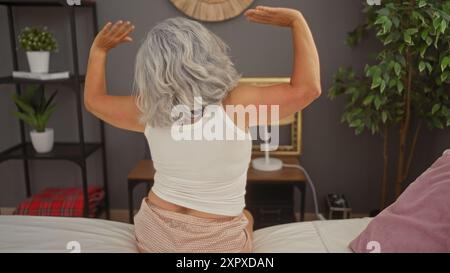 Femme mature aux cheveux gris s'étirant dans la chambre à coucher à la maison avec des plantes d'intérieur et un décor en arrière-plan Banque D'Images