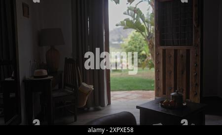 Vue intérieure d'une chambre confortable avec une porte ouverte menant à un jardin, avec une Fedora sur une table et un éclairage naturel. Banque D'Images