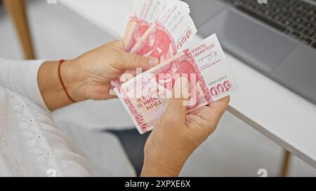 Femme mature compte la couronne islandaise dans un cadre de bureau moderne, représentant la finance et les affaires. Banque D'Images