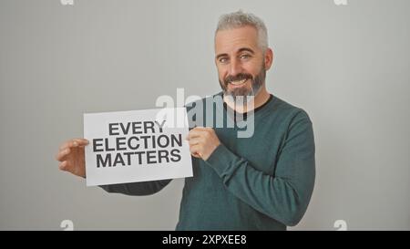 Homme barbu souriant tenant une pancarte sur les élections sur fond blanc, transmettant un message social important. Banque D'Images