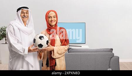 Homme musulman mature et une jeune femme tenant un ballon de football dans un salon Banque D'Images