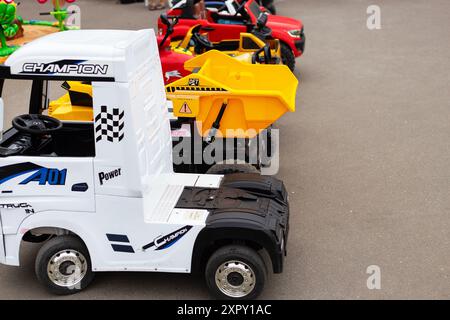 Des camions jouets colorés et des voitures autoportées alignés sur une rangée, avec un camion à benne jaune et une voiture de course rouge, parfaits pour les jeux en plein air des enfants Banque D'Images