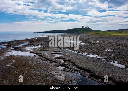 Dunstanburgh Castle et la rive rocheuse du nord à marée basse surélevée vue jour ciel bleu et nuages Banque D'Images